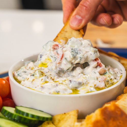 a person dipping some kind of food into a bowl with bread and cucumbers