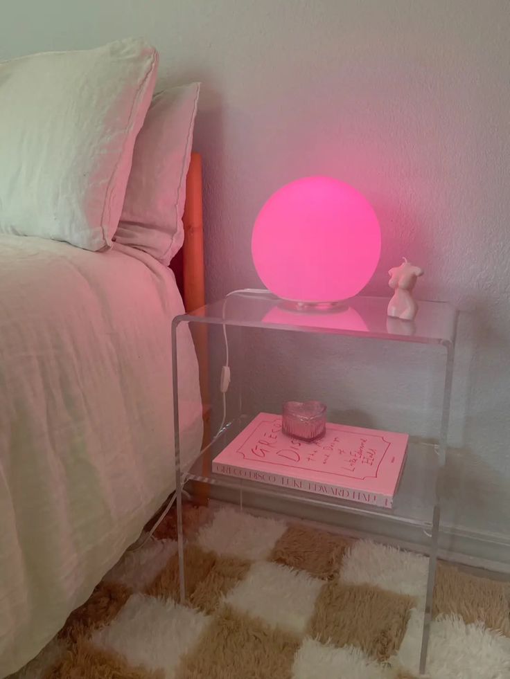 a pink lamp sitting on top of a glass table next to a bed with white sheets