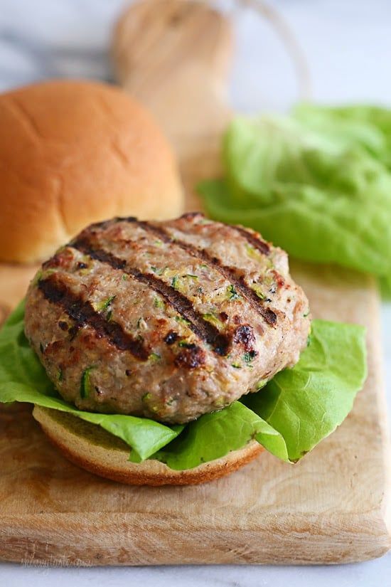 a hamburger with lettuce on a wooden cutting board next to a burger bun