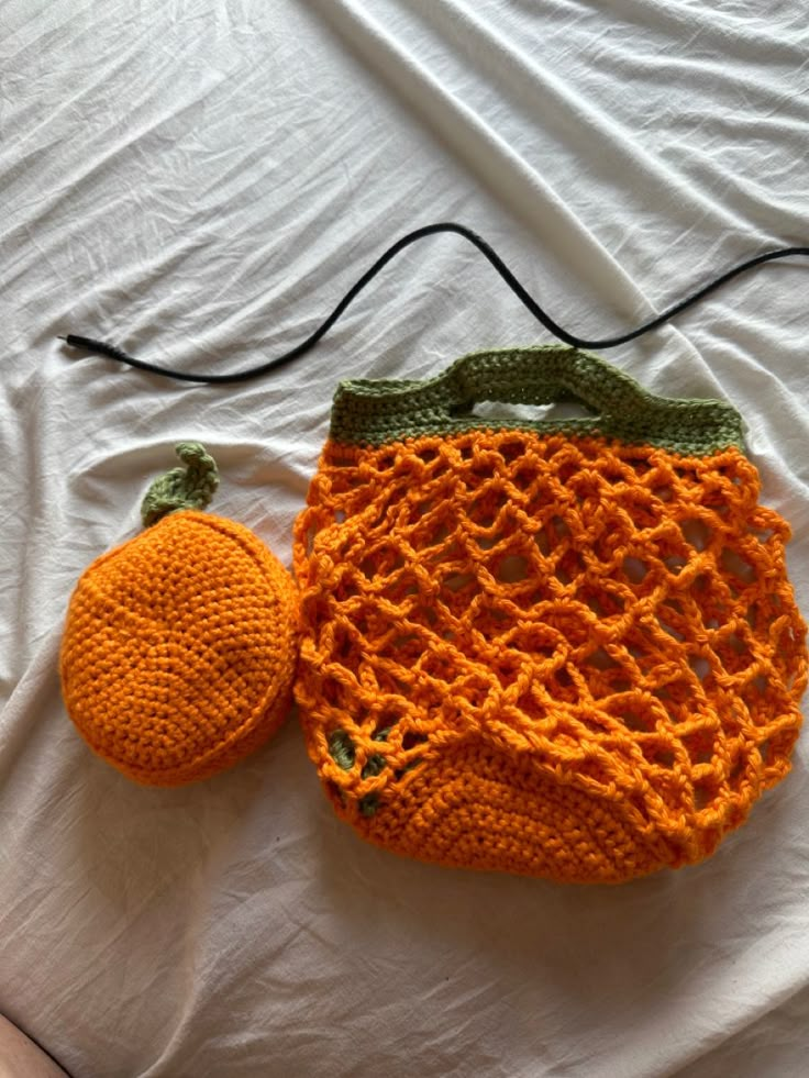 an orange and green crocheted purse sitting on top of a white bed next to a small hat