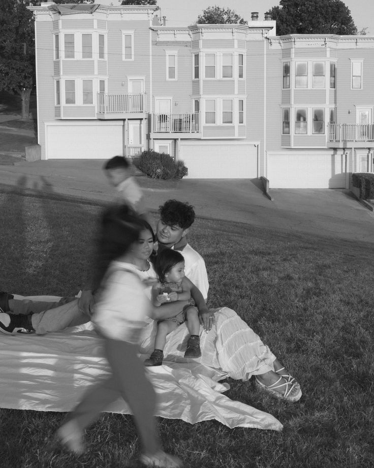 a group of people sitting on top of a grass covered field next to tall buildings