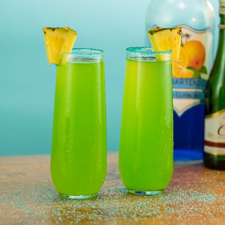 two glasses filled with green liquid next to bottles