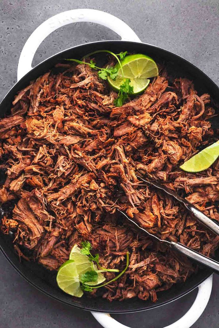 shredded beef in a skillet with limes and cilantro on the side