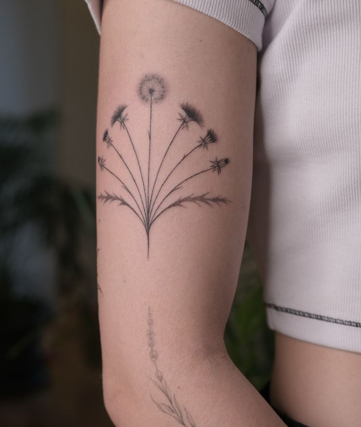 a woman's arm with a dandelion tattoo on the left side of her arm