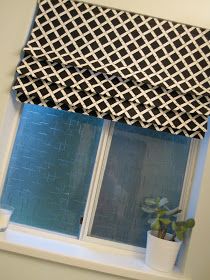 a window with a black and white patterned valance on the top, next to a potted plant