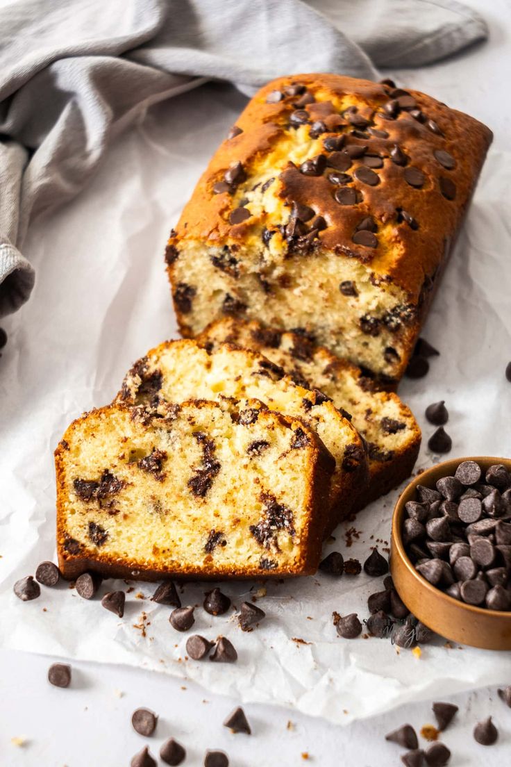 a loaf of chocolate chip banana bread next to a bowl of chocolate chips and a napkin