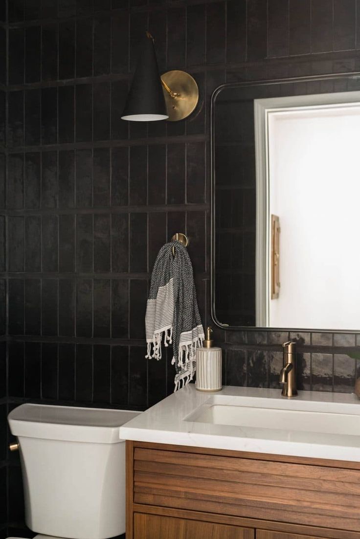 a white toilet sitting next to a bath tub under a bathroom mirror on top of a wooden cabinet