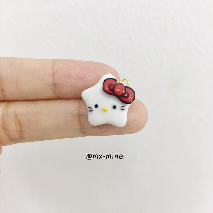 a hand holding a tiny hello kitty brooch with a red bow on it's head