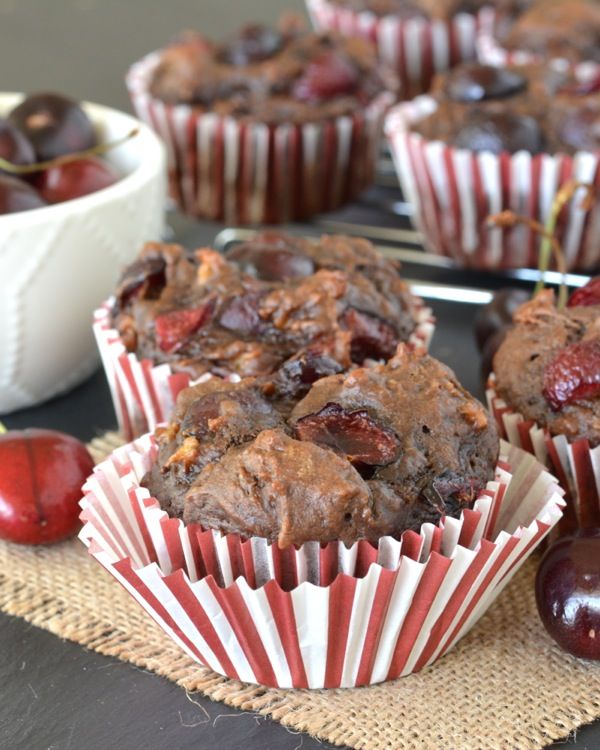 muffins with cherries in paper cups on a table next to an apple