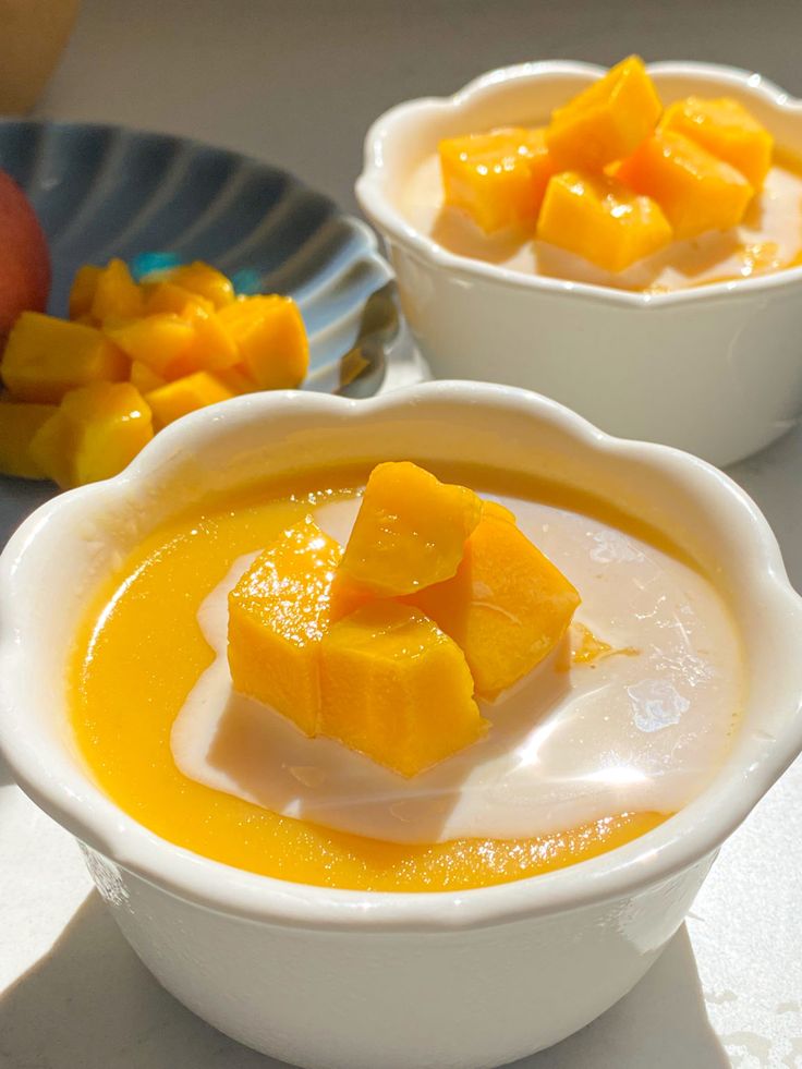 two white bowls filled with mango custard and topped with sliced pieces of mango