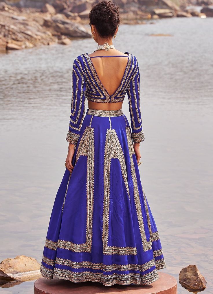 Step into the spotlight with the Ink Blue and Gold Satin Sequinned Lehenga ! Crafted with meticulous attention to detail, this bold and beautiful lehenga features exquisite hand embellishments. The inky blue color will make you stand out at any summer wedding, reception, or sangeet ceremony. The lehenga is paired with an embroidered V-neck blouse in organza satin with gorgeous full sleeves. To add a touch of elegance, the ensemble is complemented by a stunning handwork soft net dupatta. Embrace Designer Blue Fitted Lehenga, Traditional Embellished Blue Gown, Embellished Blue Sets For Reception, Party Blue Lehenga With Zari Work, Designer Fitted Blue Lehenga, Blue Hand Embellished Anarkali Set For Festive Occasions, Blue Hand Embellished Gown For Festive Occasions, Blue Gown With Resham Embroidery For Navratri, Blue Floor-length Traditional Wear With Mirror Work