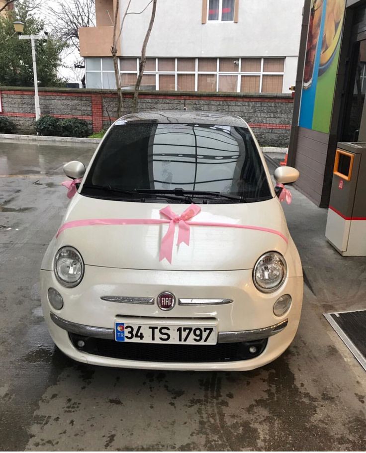 a small white car with a pink ribbon on it