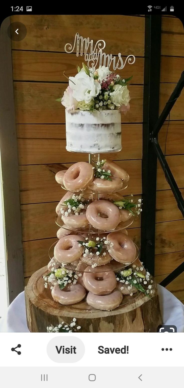 a wedding cake made out of doughnuts on top of a tree stump with flowers