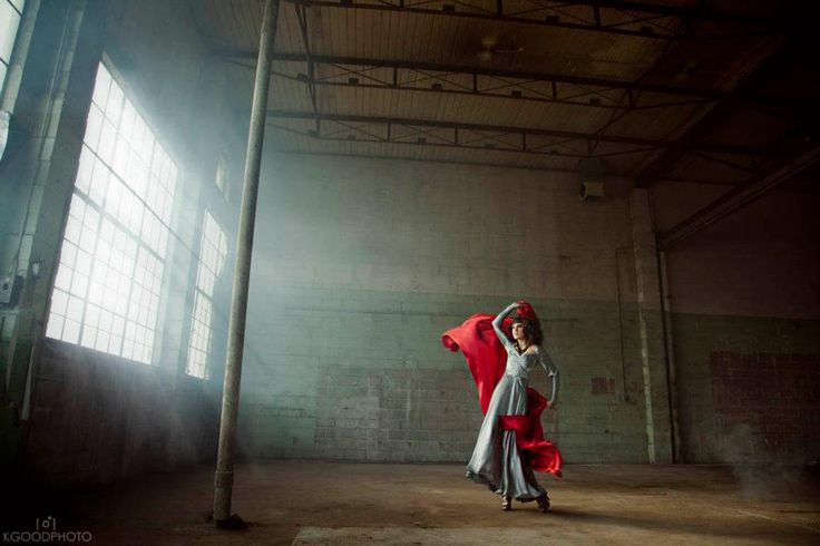 a woman is holding a red umbrella in an empty room with light coming through the windows