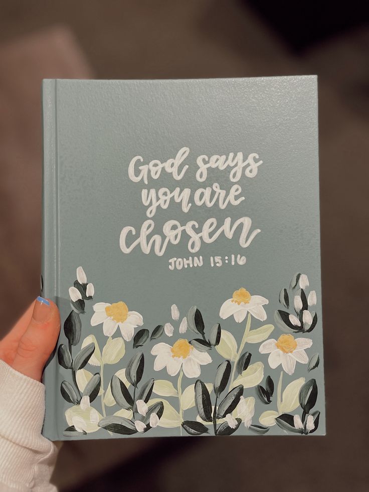 a person holding up a book with flowers on it that says god says you are chosen