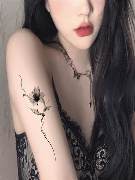 a woman with long black hair has a flower tattoo on her left arm and shoulder