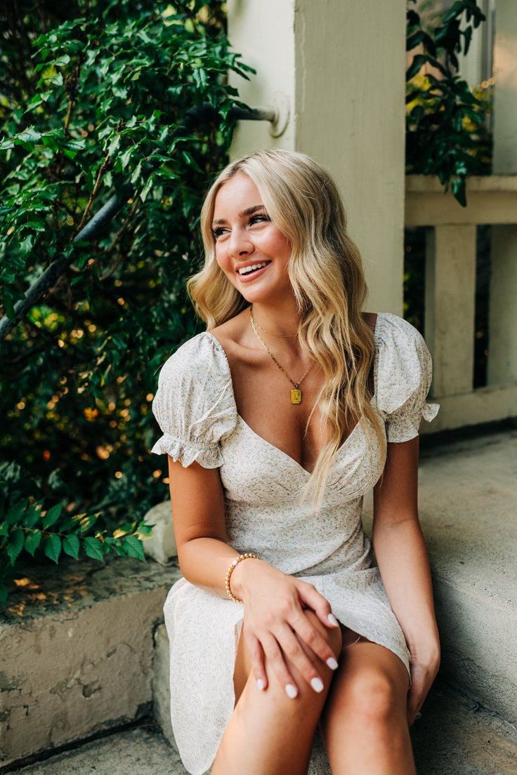 a woman sitting on the steps smiling and wearing a white dress with ruffled sleeves