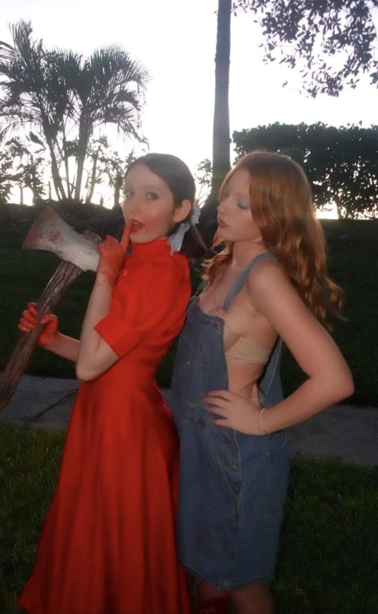 two young women standing next to each other in front of a tree and grass field