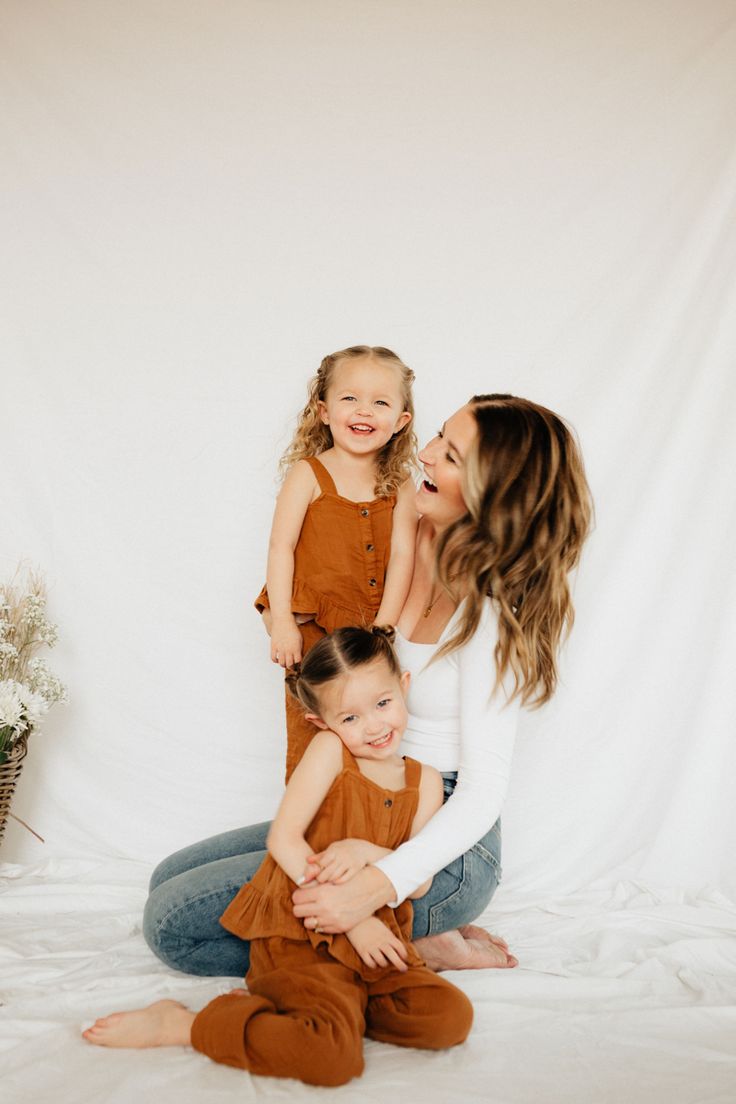 a woman sitting on the floor with her two children, both wearing brown overalls