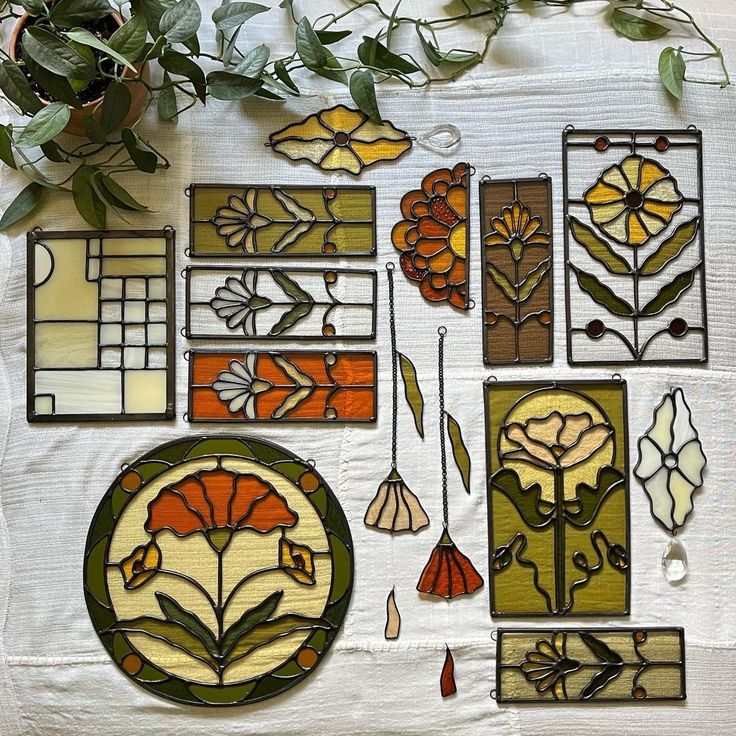 several stained glass pieces are arranged on a white tablecloth with green leaves and flowers