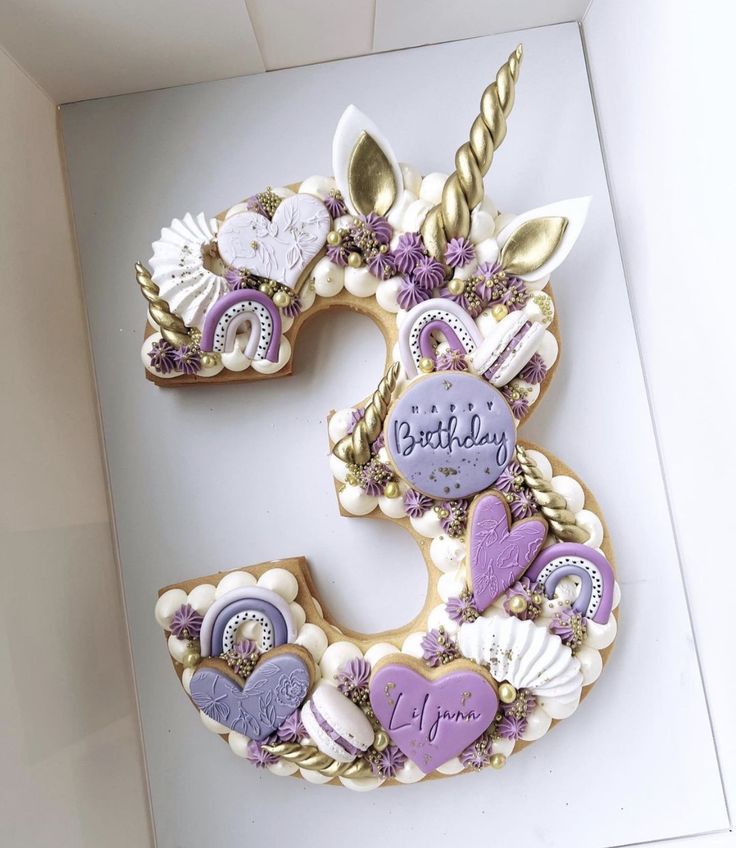 a number decorated with cookies in the shape of unicorn's head and hearts, on top of a white box