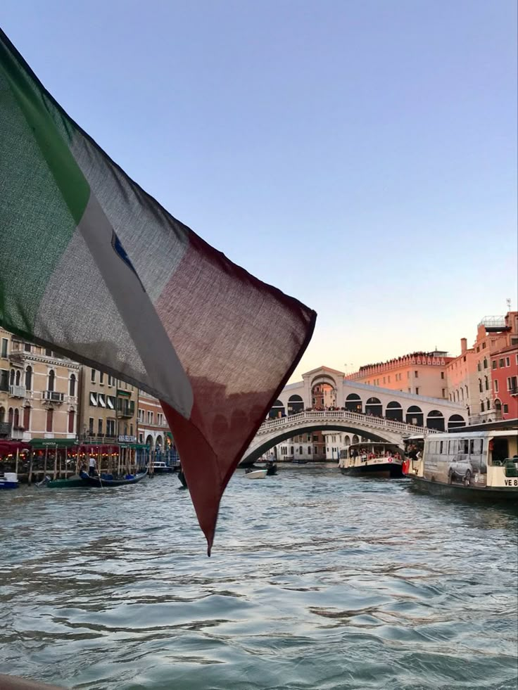 an italian flag flying in front of a bridge and buildings on the other side of a river