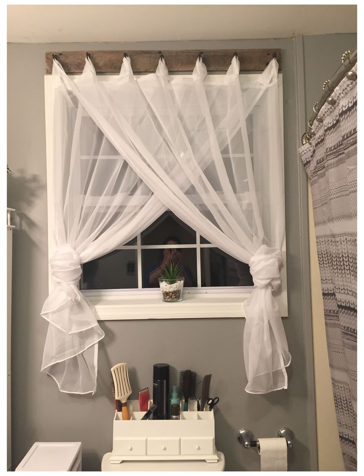 a white toilet sitting under a window next to a bathroom sink with a curtain over it