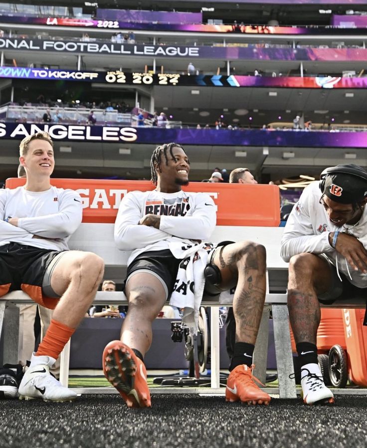 two men sitting on a bench in front of an orange and white sign at a football game