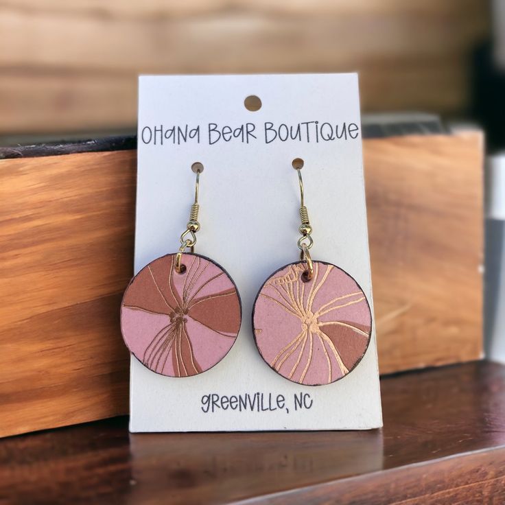 a pair of pink and gold earrings on top of a wooden table next to a sign