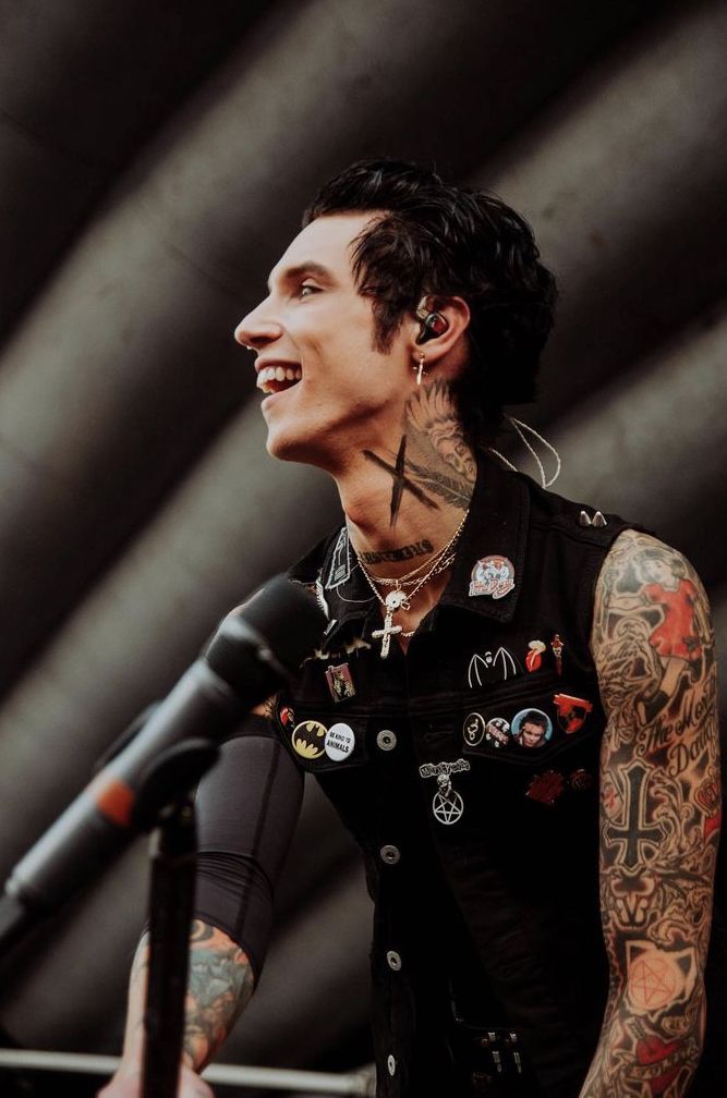 a man with tattoos and piercings standing in front of a microphone wearing a black vest