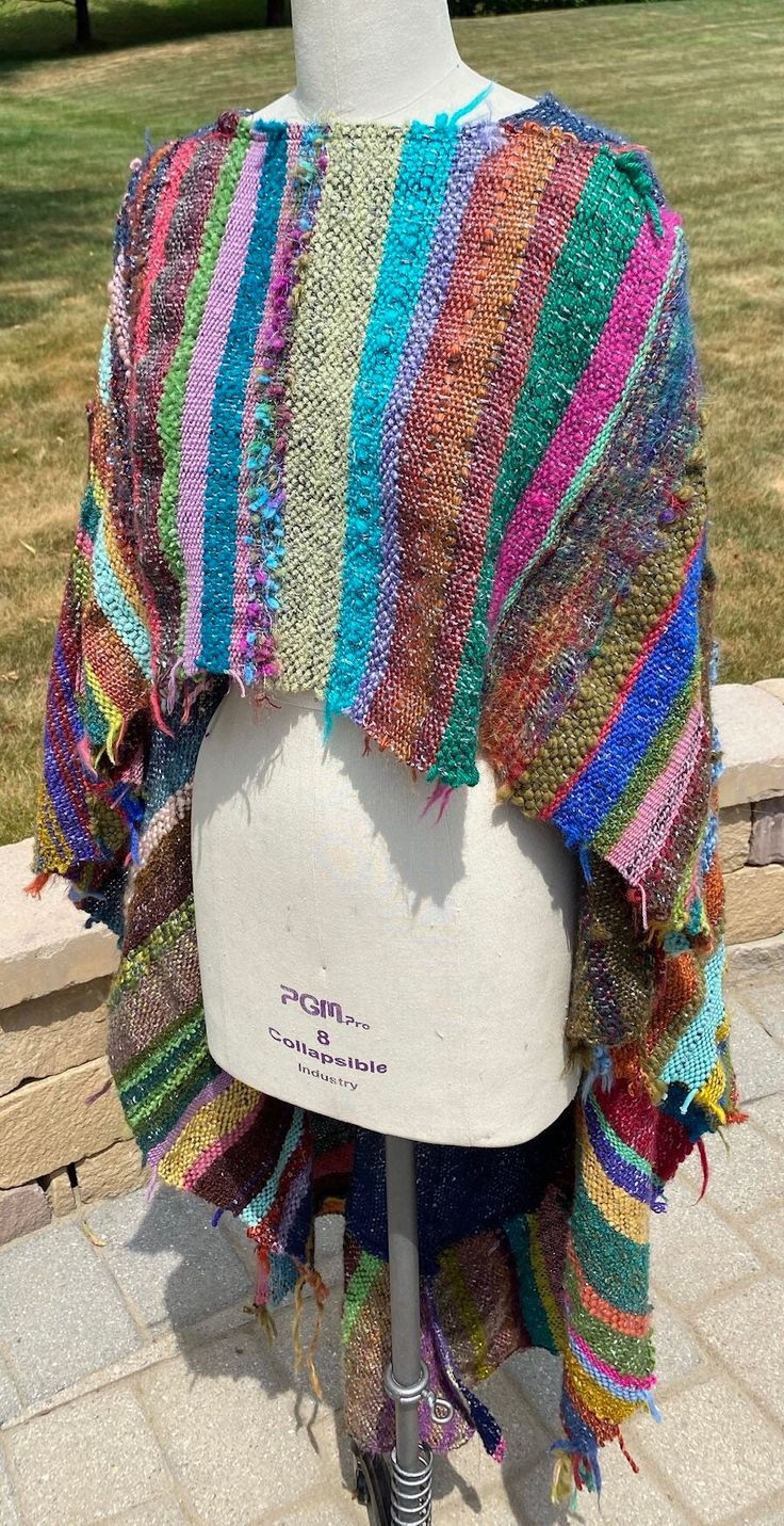 a white mannequin wearing a multicolored knitted shawl