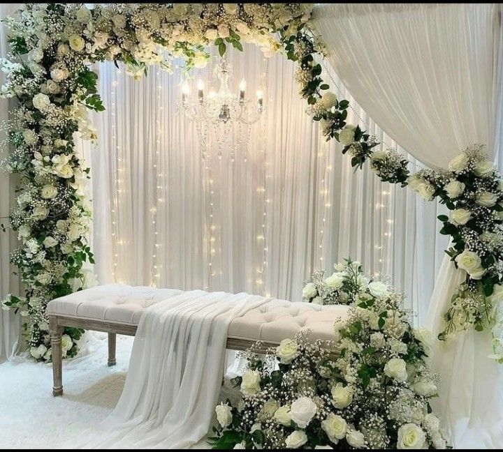 a wedding ceremony setup with white flowers and greenery on the wall, draped drapes