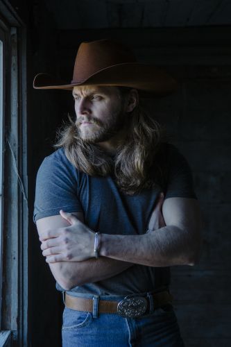 a man with long hair and a cowboy hat standing in front of an open window