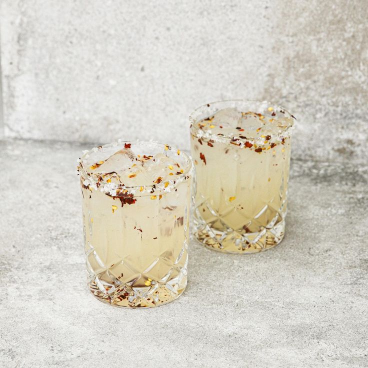 two glasses filled with drinks sitting on top of a cement floor next to each other