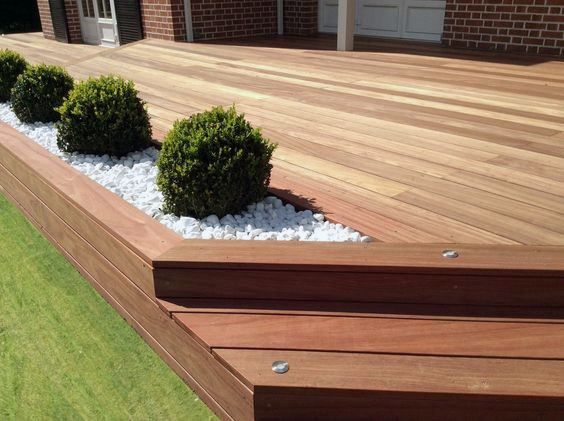 a wooden deck with white pebbles and plants in the planter area next to it