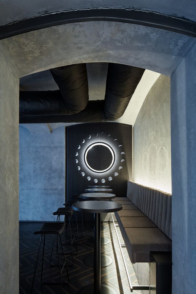 an empty restaurant with black tables and stools in front of a circular light on the wall