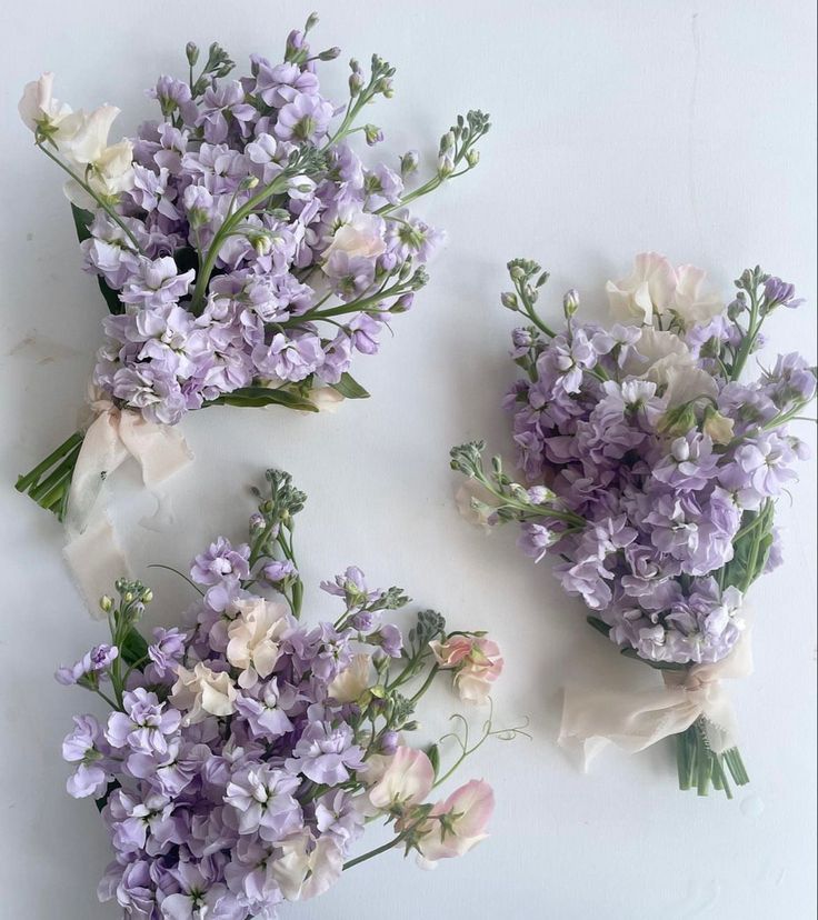 three bouquets of lavender flowers on a white surface