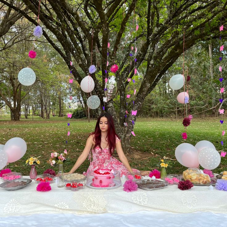 a woman sitting in front of a table with pink and white decorations on it, surrounded by balloons