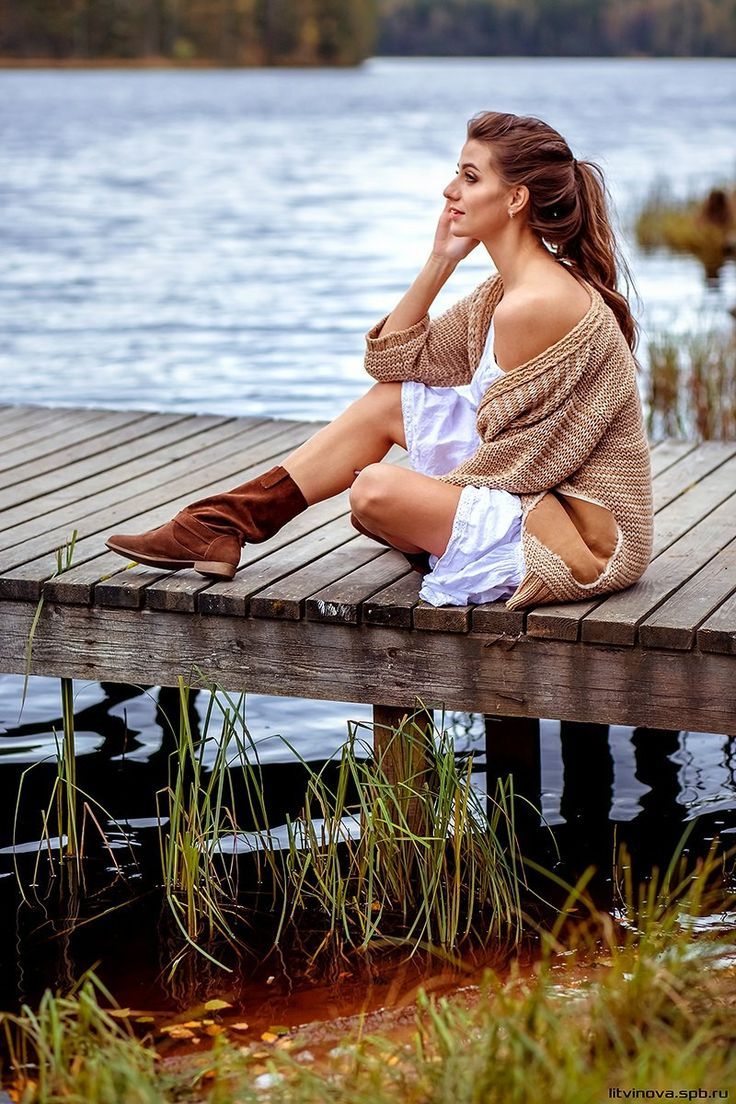 a woman is sitting on a dock by the water with her hand under her chin