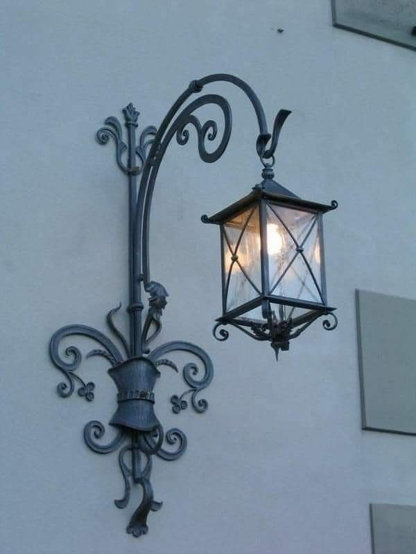 an old fashioned street lamp on the side of a building with two lights attached to it