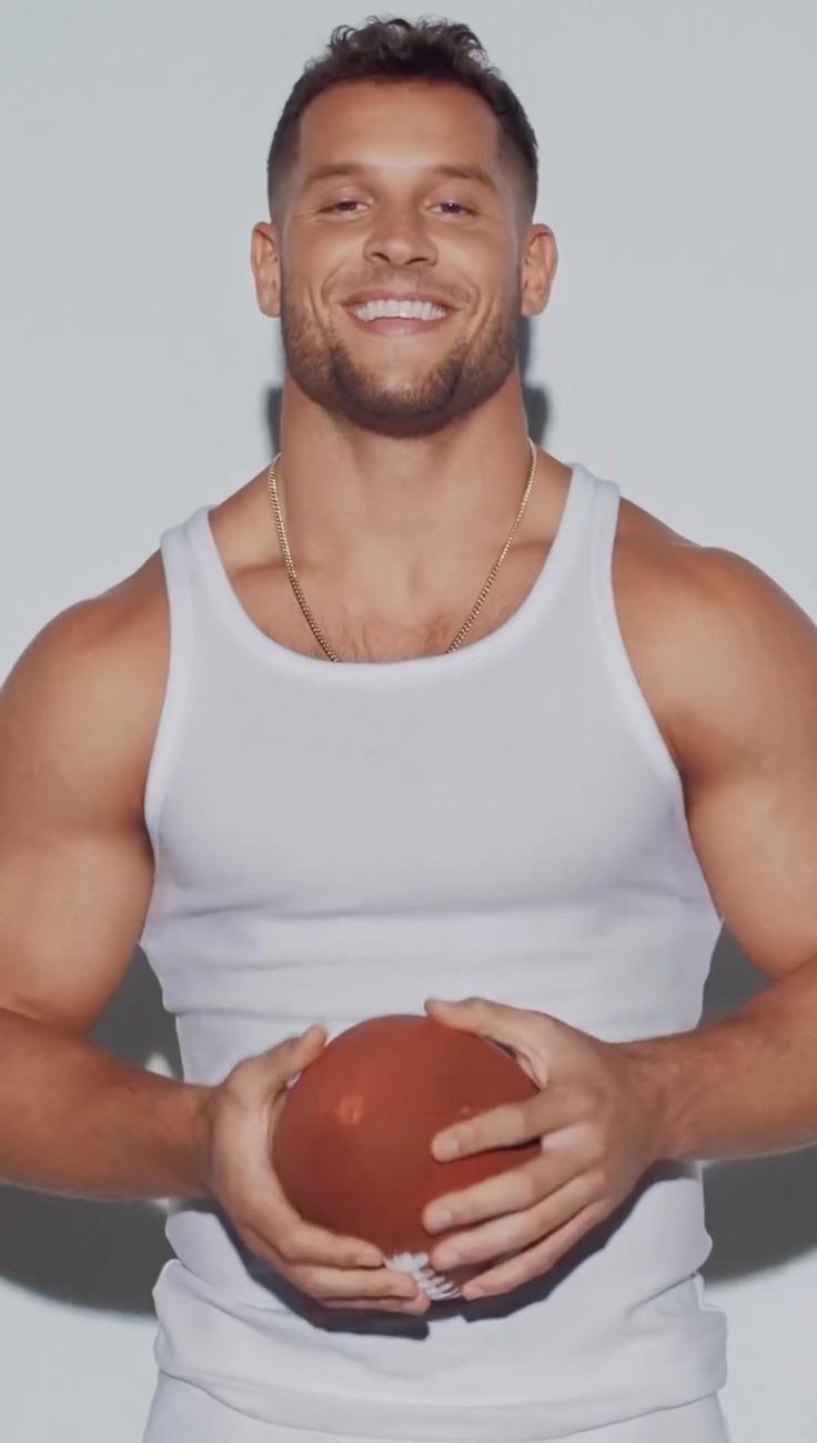 a man holding a ball in his hands and smiling at the camera while wearing a tank top