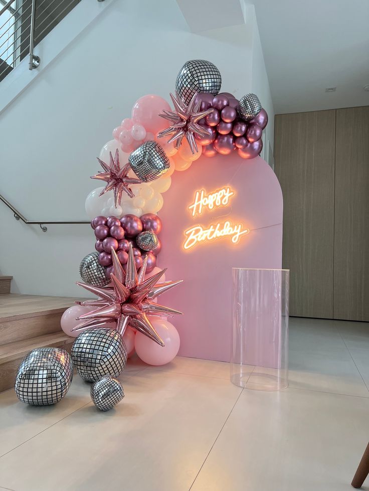 a pink and silver balloon arch with happy birthday balloons on it in front of stairs