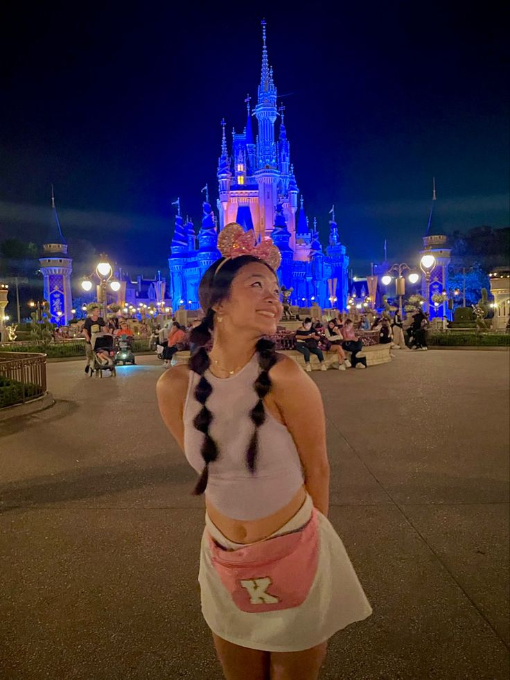 a woman standing in front of a castle at night with her hand on her hip