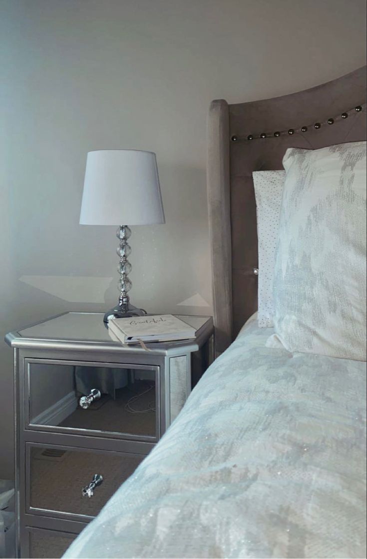 a bed with white sheets and pillows next to a lamp on a nightstand in a bedroom