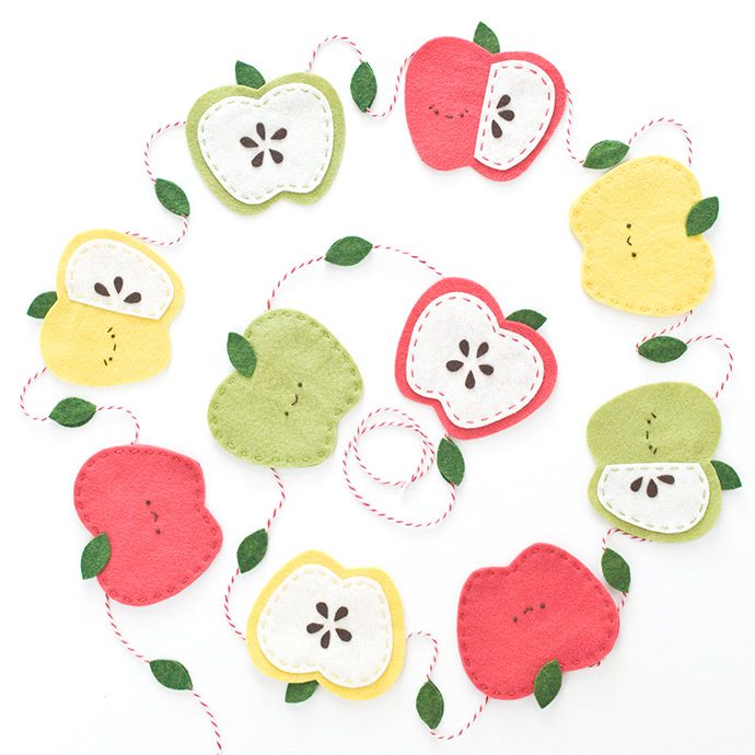 felt apples and pears hanging from twine on white background with green leaves in center