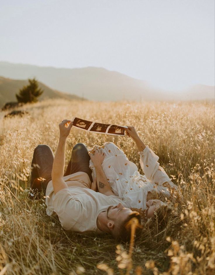 a man and woman laying on the ground in a field holding up an old photo frame