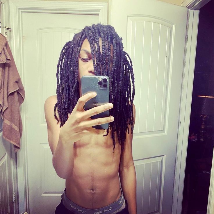 a man with dreadlocks is taking a selfie in the mirror while holding his cell phone