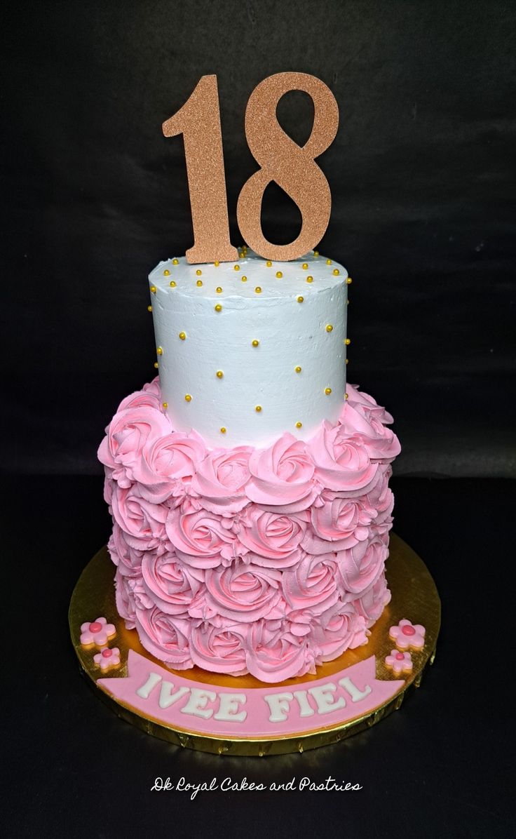 a white and pink cake with gold numbers on it's top, sitting on a plate