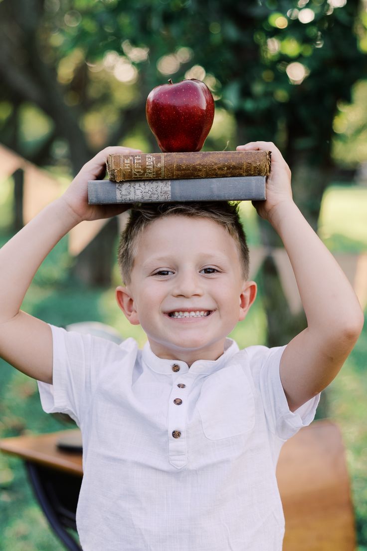 a young boy holding an apple on top of a book