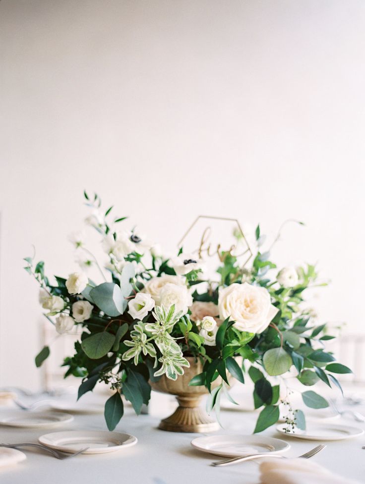 a vase filled with white and green flowers on top of a table covered in plates